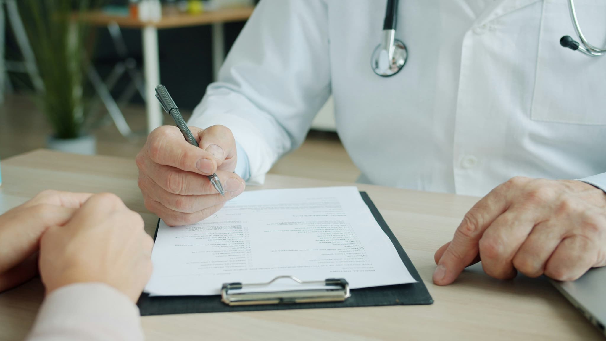 Médico con bata blanca revisando un formulario médico con un paciente durante una consulta preoperatoria.
